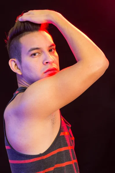 Homme hispanique portant rouge rayé noir singulet posant avec une expression faciale grave, montrant bras droit couvrant la bouche, angle de profil — Photo