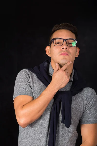 Uomo ispanico con camicia stretta, maglione sulle spalle e occhiali dall'aspetto sofisticato fotocamera frontale, sfondo nero — Foto Stock