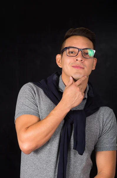 Hispánský muž nosí těsné tričko, svetr přes ramena a brýle hledají sofistikované čelí fotoaparát, černé pozadí — Stock fotografie