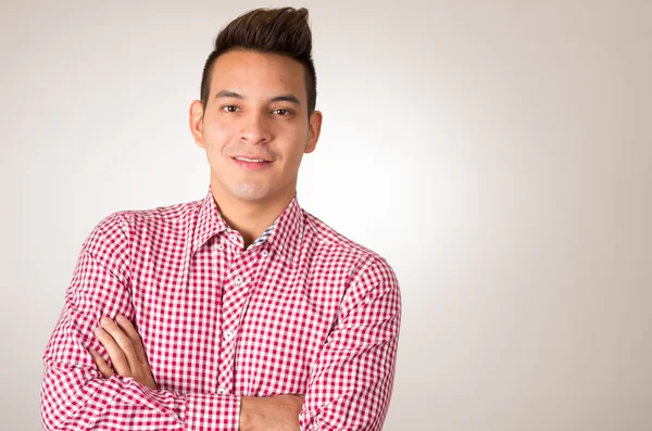 Hispânico masculino vestindo vermelho branco camisa posando sorrindo com braços cruzados vazio fundo — Fotografia de Stock