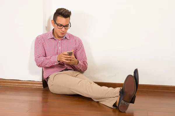 Hispanischer Mann mit rotweißem Hemd sitzt auf Holzboden vor leerem Hintergrund — Stockfoto