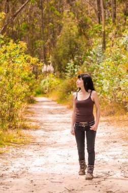 Pretty brunette with tattoos wearing rock inspired clothing walking on dirt road in forest environment enjoying nature