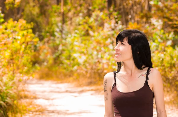 Jolie brune avec des tatouages portant des vêtements inspirés de la roche marchant sur un chemin de terre dans un environnement forestier appréciant la nature — Photo