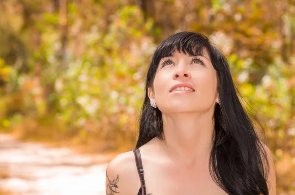 Jolie brune tatouée portant des vêtements inspirés de la roche marchant sur un chemin de terre dans un environnement forestier profitant de la nature, face à la caméra levant les yeux vers le ciel — Photo