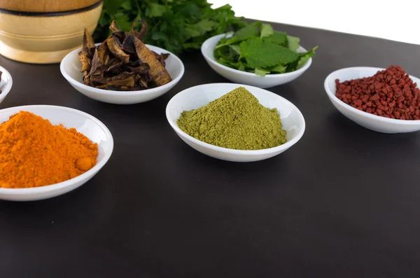 Beautiful colorful display of different spices green orange brown in white bowls, shot from above side angle, grey background — ストック写真