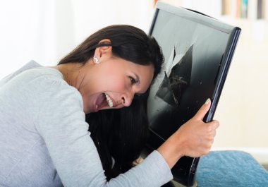 Brunette hispanic model holding up broken black computer screen while smashing her head into it