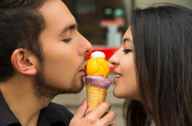 Cute hispanic couple sharing ice cream cone and enjoying each others company in outdoors environment