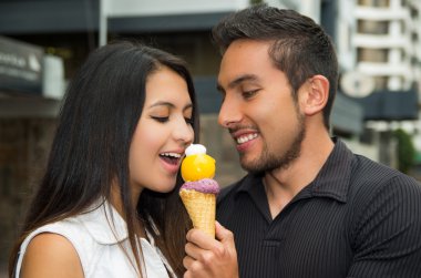 Cute hispanic couple sharing ice cream cone and enjoying each others company in outdoors environment