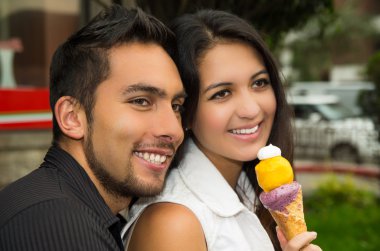 Cute hispanic couple sharing ice cream cone and enjoying each others company in outdoors environment