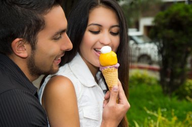 Cute hispanic couple embracing while sharing ice cream cone and enjoying each others company in outdoors environment