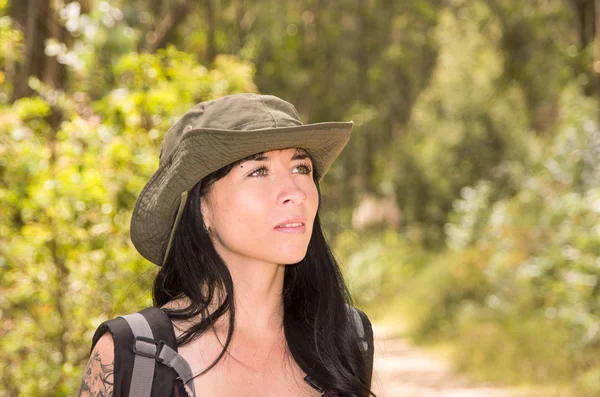 Adventurous brunette trekking in forest environment wearing green safari hat and backpack — Stok fotoğraf