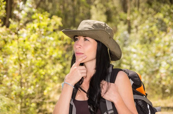 Adventurous brunette trekking in forest environment wearing green safari hat and backpack — Stok fotoğraf
