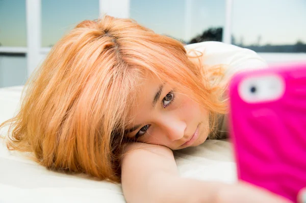 Mulher muito jovem, adolescente deitado aconchegante na cama segurando telefone celular rosa levando selfie — Fotografia de Stock