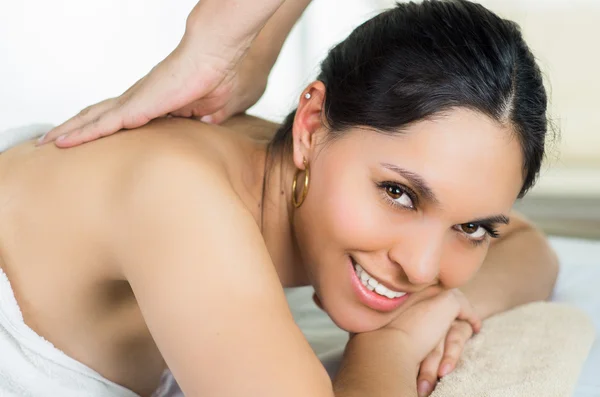 Hispanic brunette model getting massage spa treatment, white towel covering upper body lying horizontal smiling to camera — Zdjęcie stockowe