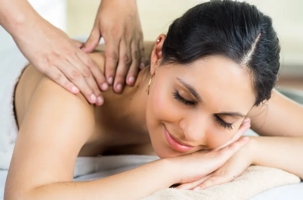 Hispanic brunette model getting massage spa treatment, white towel covering upper body lying horizontal smiling to camera — 스톡 사진