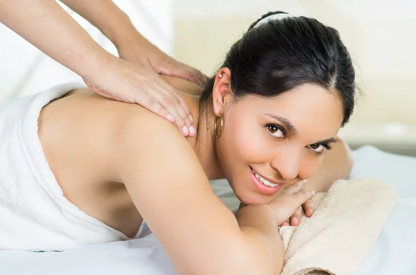 Hispanic brunette model getting massage spa treatment, white towel covering upper body lying horizontal smiling to camera — 图库照片