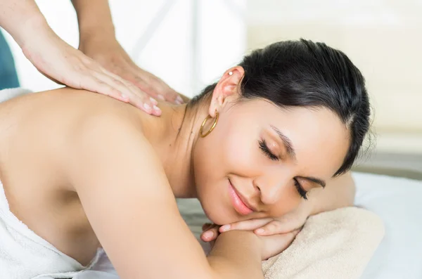 Hispanic brunette model getting massage spa treatment, white towel covering upper body lying horizontal smiling to camera — 图库照片