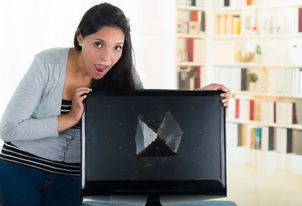 Brunette female looking over broken computer screen with shocked facial expression on her face — Stock fotografie