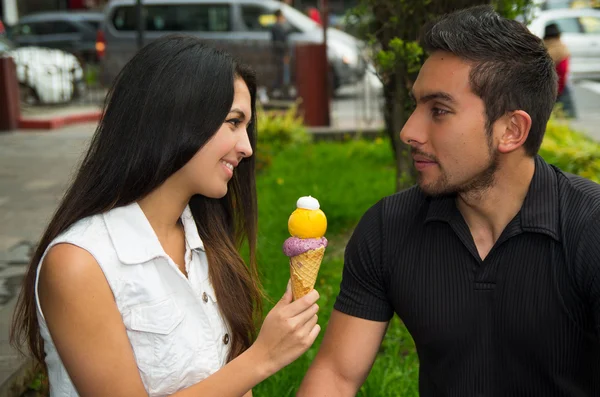 Linda pareja hispana compartiendo cono de helado y disfrutando de la compañía de los demás en el ambiente al aire libre — Foto de Stock