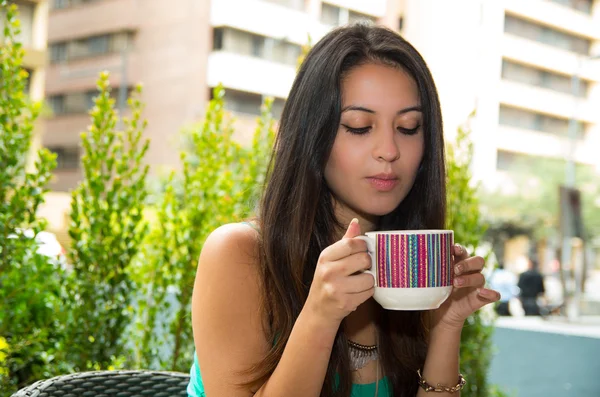 Modelo muito morena vestindo singlet turquesa sentado à mesa da cafetaria lendo papel enquanto desfruta de café — Fotografia de Stock