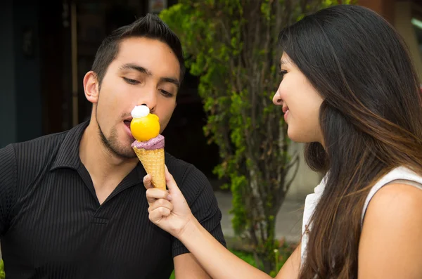 Cute hispanic couple embracing while sharing ice cream cone and enjoying each others company in outdoors environment — 스톡 사진