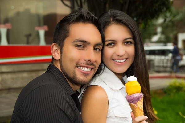 Cute hispanic couple embracing while sharing ice cream cone and enjoying each others company in outdoors environment — Stockfoto