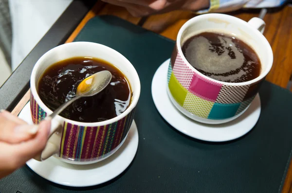 Closeup two colorful cups of coffe sitting on restaurant table with hand holding spoon in one cup — Stockfoto