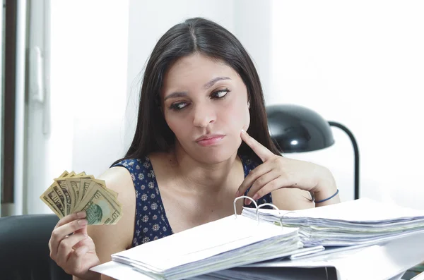 Hispanische brünette Bürofrau sitzt am Schreibtisch mit geöffnetem Papierarchiv und hält mehrere Zehn-Dollar-Scheine in der Hand — Stockfoto