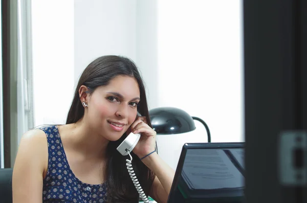 Hispanische Brünette sitzt am Schreibtisch und telefoniert lächelnd mit positiver Einstellung — Stockfoto