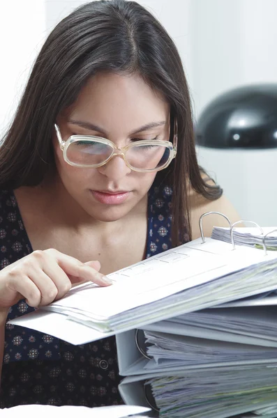 Hispanic brunette office woman wearing glasses working on paper files archives while sitting by desk — Stock fotografie