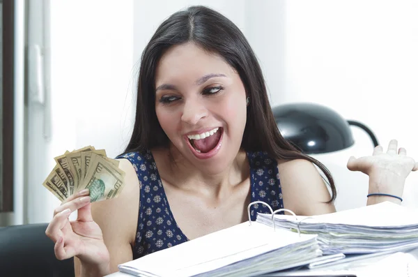 Hispanische brünette Bürofrau sitzt am Schreibtisch mit geöffnetem Papierarchiv und hält lächelnd mehrere Zehn-Dollar-Scheine in der Hand — Stockfoto