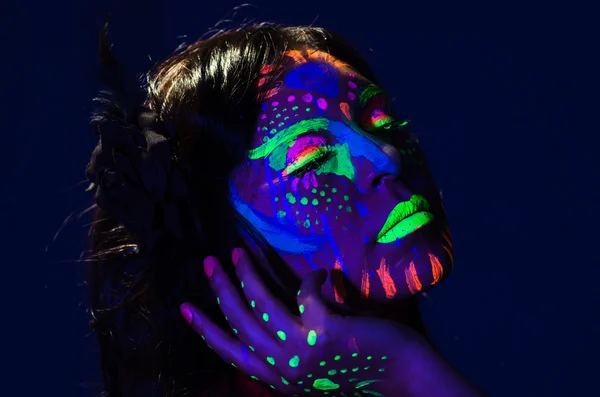 Mulher headshot vestindo brilho impressionante em tinta facial escura, azul com base em outras cores de néon e fundo abstrato obscuro, câmera de frente — Fotografia de Stock