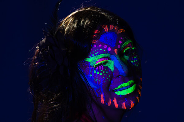 Headshot woman wearing awesome glow in dark facial paint, blue based with other neon colors and obscure abstract background, facing camera