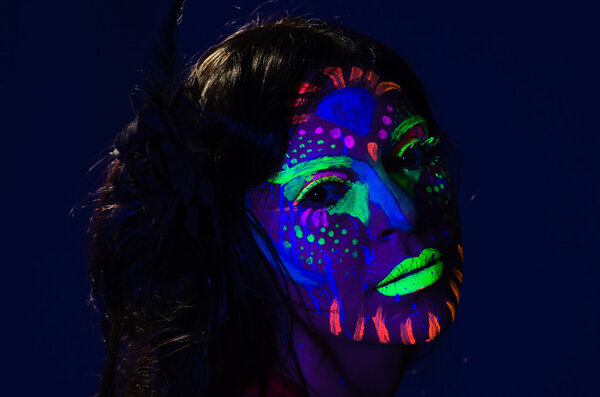 Headshot woman wearing awesome glow in dark facial paint, blue based with other neon colors and obscure abstract background, facing camera