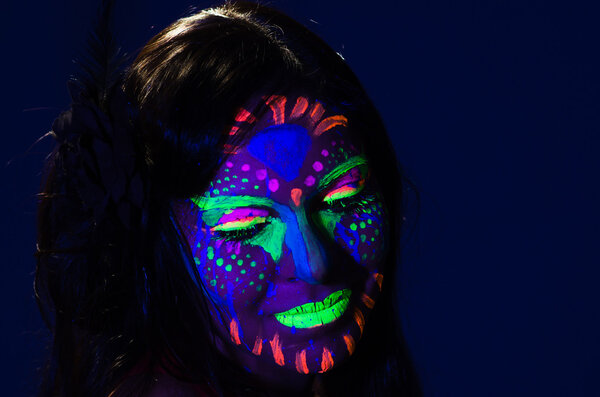 Headshot woman wearing awesome glow in dark facial paint, blue based with other neon colors and obscure abstract background, facing camera