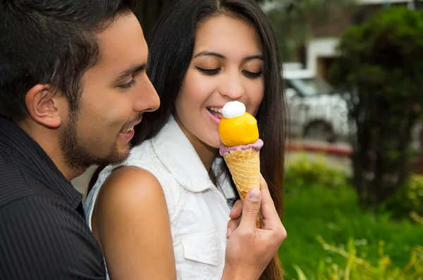 Cute hispanic couple embracing while sharing ice cream cone and enjoying each others company in outdoors environment — Stock Photo, Image