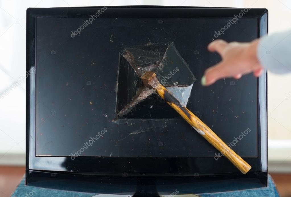 Standard hammer stuck in computer screen after smashing it, hand reaching for it