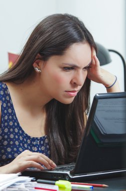 Hispanic brunette sitting by office desk working on computer with occupied and worried facial expression