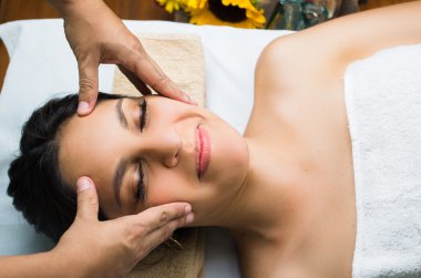 Hispanic brunette model getting massage spa treatment, hands working on massaging womans head and face with eyes closed