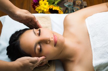 Hispanic brunette model getting massage spa treatment, hands working on massaging womans head and face with eyes closed
