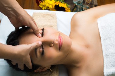Hispanic brunette model getting massage spa treatment, hands working on massaging womans head and face with eyes closed