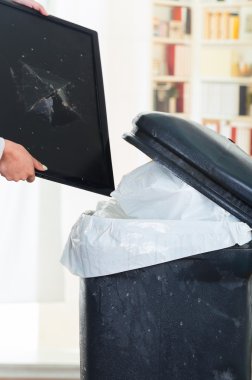 Broken computer screen going into large black trash dumpster