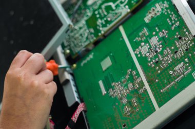 Hands working with electronic circuit board from broken computer screen using small screwdriver