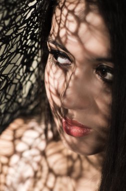 Headshot brunette model using patterned shadows as artistic effect on face while posing
