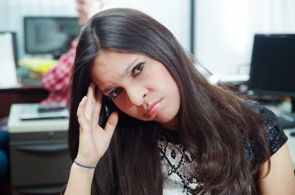 Hispanische brünette Büroangestellte am Schreibtisch sitzend, den Kopf in die Hände geneigt und müde wirkend — Stockfoto