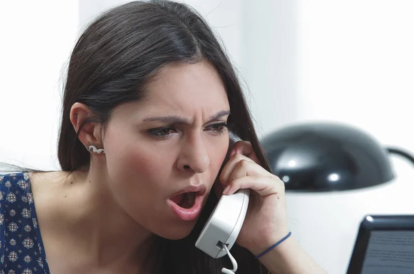 Morena hispânica sentada na mesa do escritório conversando por telefone com expressão facial ocupada e preocupada — Fotografia de Stock