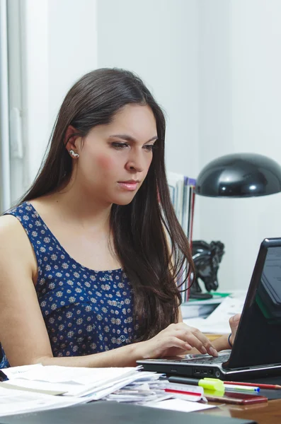 Hispanic brunette office woman sitting by desk and working on computer with positive attitude smiling — Stok fotoğraf