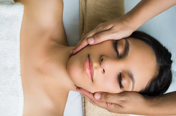 Modelo morena hispana recibiendo tratamiento de spa de masaje, manos trabajando en el masaje de la cabeza y la cara de las mujeres con los ojos cerrados — Foto de Stock