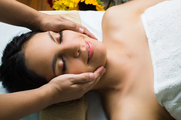 Modelo morena hispana recibiendo tratamiento de spa de masaje, manos trabajando en el masaje de la cabeza y la cara de las mujeres con los ojos cerrados — Foto de Stock