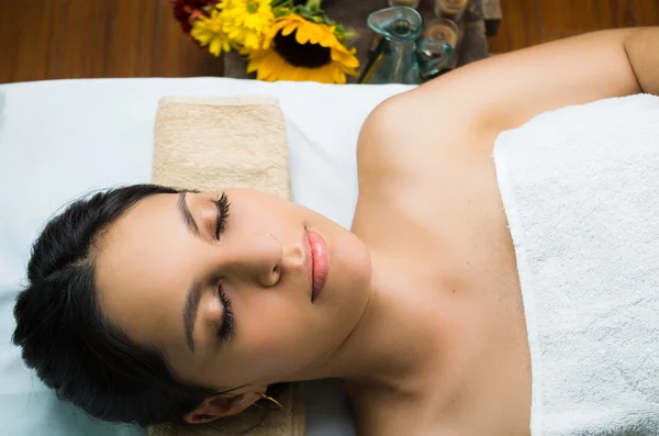 Hispanic brunette model getting massage spa treatment, woman lying with white towel and eyes closed, shot from above